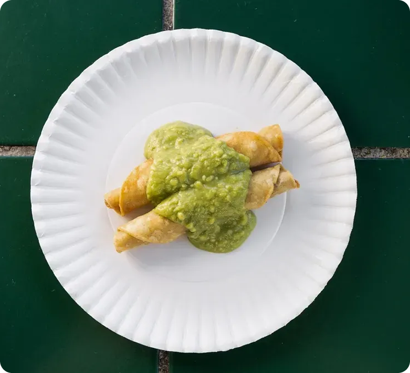 Taquitos with green sauce on paper plate.